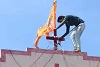 Dieser Mann montiert eine safranfarbene Fahne mit dem Bild des Ram-Tempels auf einem Kirchendach. csi